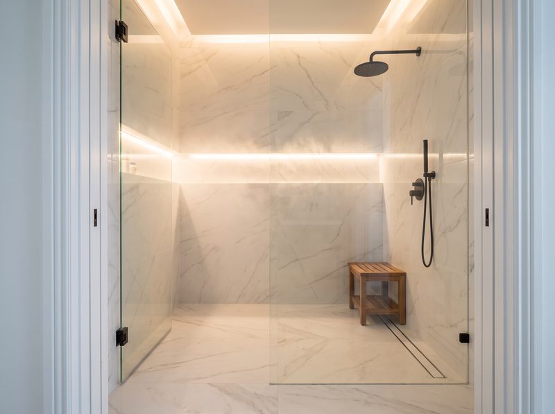 Marble-look porcelain shower with black fixtures and teak bench