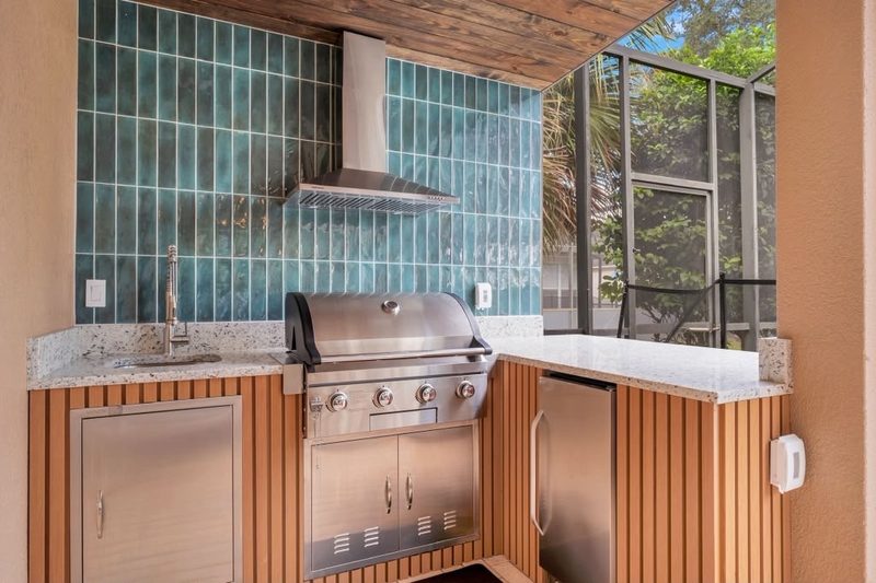 Finished outdoor summer kitchen with green tile backsplash, grill and PVC slat panels
