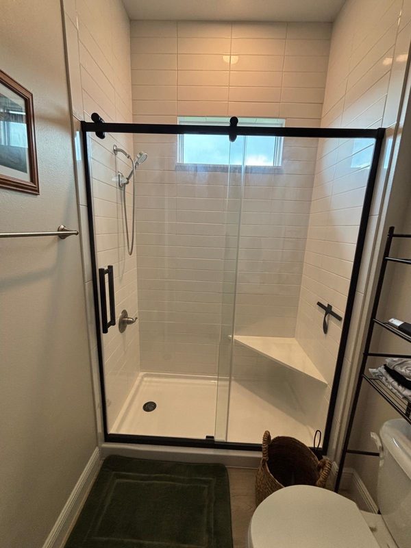 Finished walk-in shower with white tile and black-frame glass door