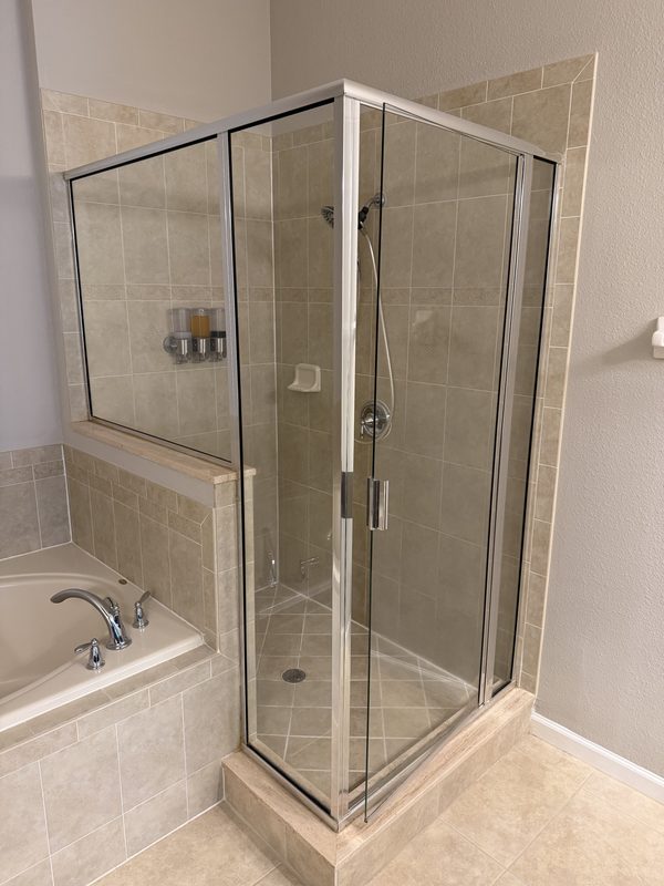 Same shower before, with framed glass and beige tile